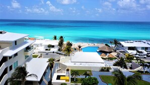 A resort with a pool, palm trees, and a view of the ocean. - New Beachfront PH at Brisas By The Spot (Cancun)