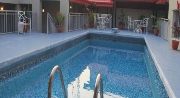 A swimming pool with a metal ladder, surrounded by potted plants and outdoor furniture. - The Ambassadors Hotel (Lagos)