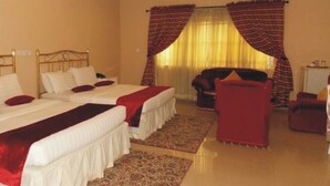 Una habitación de hotel con dos camas, un sillón rojo y una mesita.