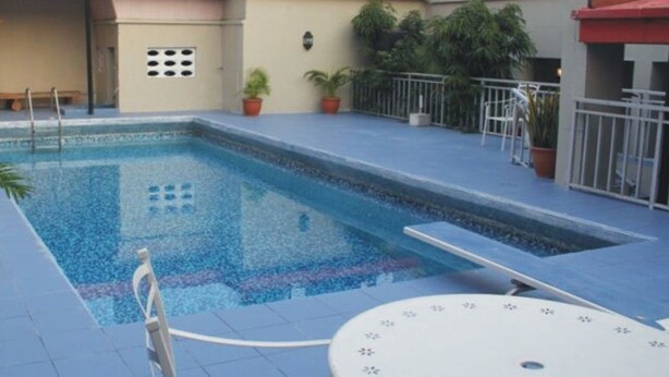 Una piscina rectangular con un borde de baldosas, rodeada de plantas en macetas y una barandilla de metal.