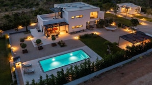 Una casa moderna de dos pisos amb piscina, zona d'estar a l'exterior i un pati ben il·luminat.