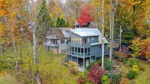 Een groot, twee verdiepingen tellend huis met een balkon, omgeven door herfstkleuren.