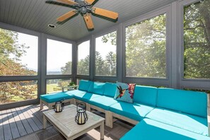 A covered porch with a blue sofa, a wooden table, and a ceiling fan.