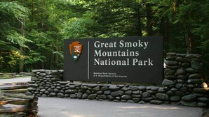 Bordje voor Great Smoky Mountains National Park, met een stenen muur en een bebost landschap.