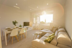 A modern living room with a sofa, dining table, chairs, and a TV.