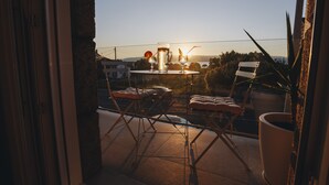 A balcony with a table set for two, a potted plant, and a view of the sunset. - Balcony at Arousa - Upscale Getaway + Patio (Villagarcía de Arosa)