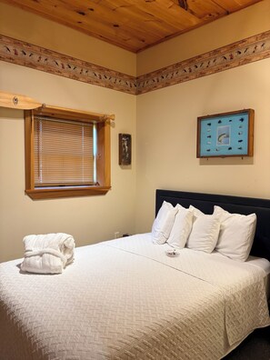 A bedroom with a bed, a window with blinds, a framed picture on the wall, and a towel on the bed.