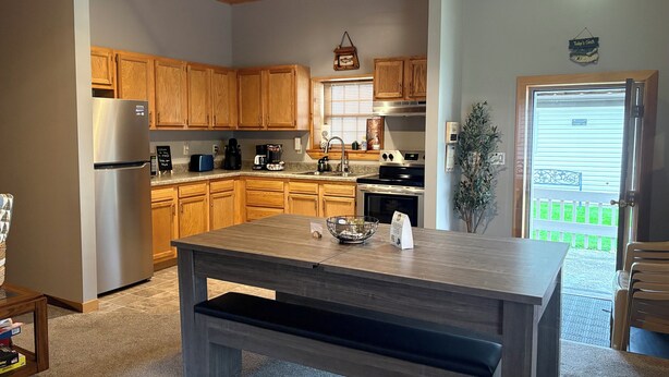 A kitchen with wooden cabinets, a stainless steel refrigerator, a built-in oven, and a dining area with a bench. - Stay In Ohiopyle, Hot tub & Pool Table - Closest to the GAP trail (Ohiopyle)