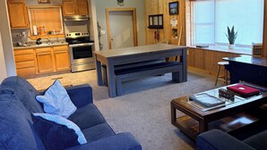 A cozy living room with a sofa, a coffee table, a dining table, and a kitchen area with wooden cabinets and appliances. - Stay In Ohiopyle, Hot tub & Pool Table - Closest to the GAP trail (Ohiopyle)