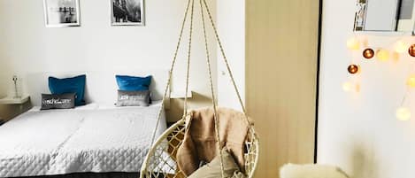 A bedroom with a hanging chair, a bed with pillows, a chandelier, and wall art.