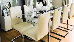 Un espace de salle à manger moderne avec une table en verre, des chaises blanches, un lustre et un mur d’accent noir.