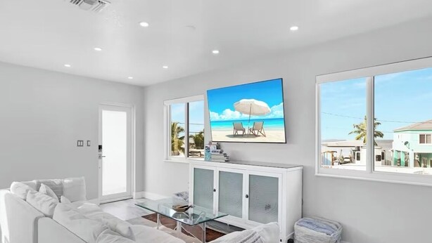 A modern living room with a white sofa, a glass coffee table, and a large beach-themed painting above it. - Amazing Sunsets, Bay Breezes in the beautiful Florida Keys (Key Largo)