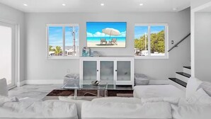 A modern living room with a large TV, white sofas, a glass coffee table, and a view of the beach through the windows. - Amazing Sunsets, Bay Breezes in the beautiful Florida Keys (Key Largo)