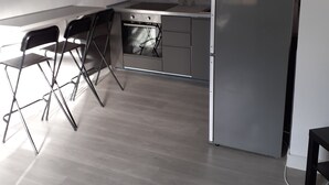 Una cocina con un refrigerador de acero inoxidable, una estufa a gas y un horno empotrado. Hay sillas plegables y piso de madera.