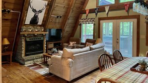 Ein gemütliches Wohnzimmer im Loft-Stil mit Kamin aus Stein, einem Fernseher, einer Couch und einem Essbereich mit kariertem Tischläufer.