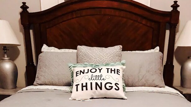 A bed with a wooden headboard, two bedside lamps, and a decorative pillow with the text "ENJOY THE little THINGS". - 2BR Pet-Friendly Getaway on Ursuline in NOLA (New Orleans)
