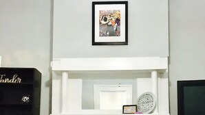 A living room with a fireplace, a framed picture above it, and a television to the right. - 2BR Pet-Friendly Getaway on Ursuline in NOLA (New Orleans)