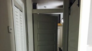 A narrow hallway with wooden flooring and white walls, leading to a room with a white door. - 2BR Pet-Friendly Getaway on Ursuline in NOLA (New Orleans)