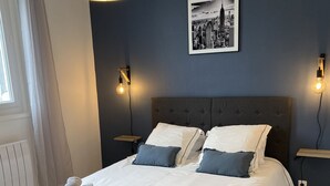 Ein ordentlich bezogenes Bett mit weißen Leinentüchern und aufgerollten Handtüchern, eine dunkelblaue Wand und ein Stadtbild darüber.