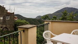 A balcony with a table and chairs, overlooking a mountainous landscape.