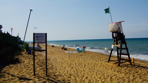 Ein Strand mit einem Rettungsturm, einem Schild, der eine Fahrrinne kennzeichnet, und Personen im Wasser.