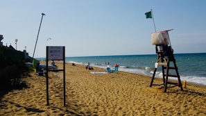 A beach with a lifeguard tower, a sign indicating a nautical channel, and people enjoying the beach.