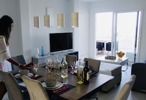 A modern dining area with a large table set for a meal, a flat-screen TV, and a balcony with outdoor seating.