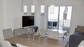 Ein moderner Essbereich mit einem Holztisch, grau gepolsterten Stühlen und einem Flachbildfernseher auf einem grauen Schrank.