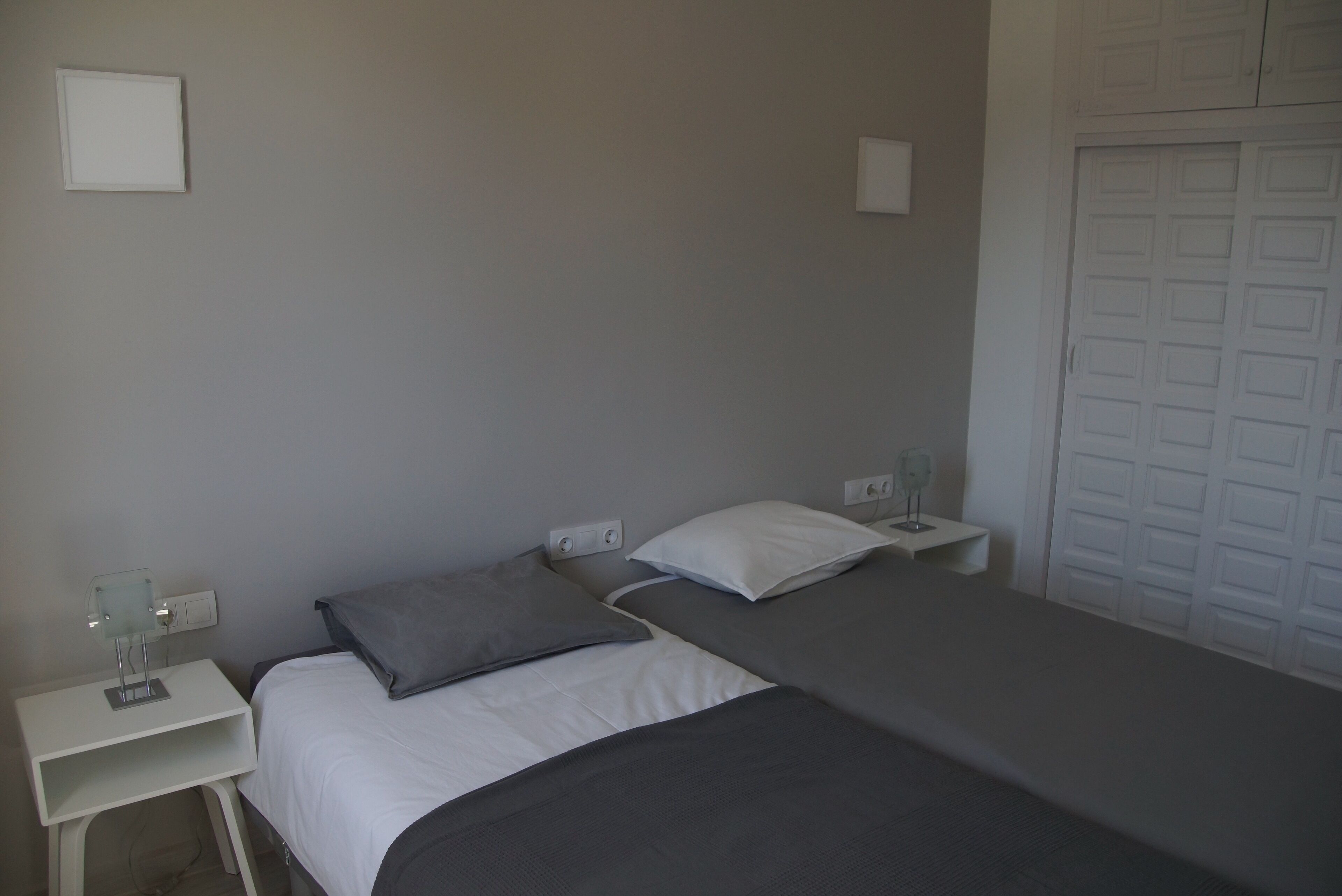 Une chambre avec deux lits, une table de chevet, une lampe fixée au mur et un placard.