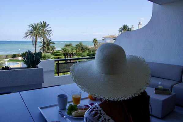 A balcony with a view of the ocean, a white hat, a glass of orange juice, and a plate of food.