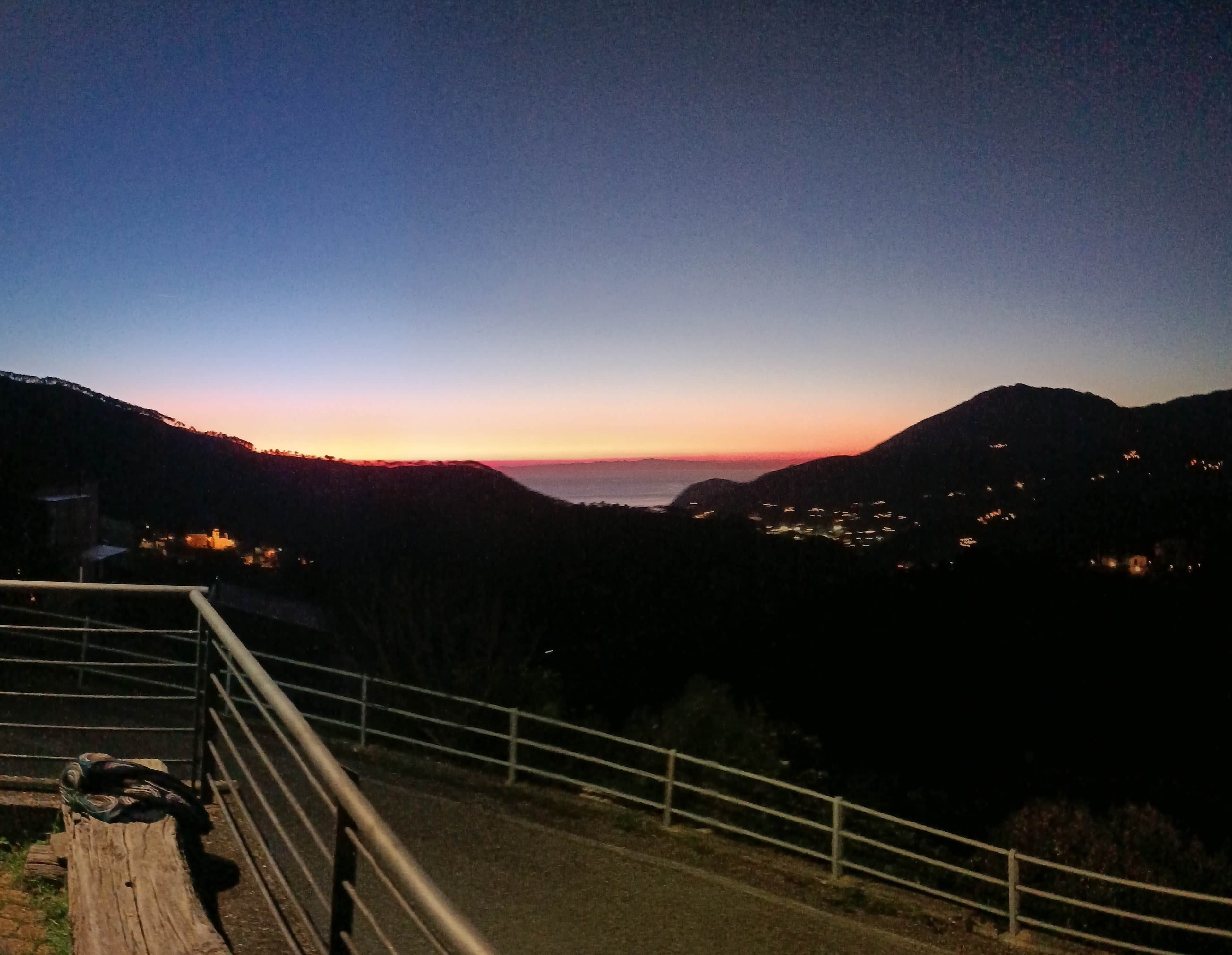 Vista noturna de uma paisagem montanhosa com estrada e guarda-corpo.