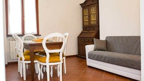 A dining area with a wooden table and white chairs, a cabinet, and a grey sofa. - Holiday Home Tra Le Mura "Timo"-Levanto 5 Terre- (Chiesa Nuova, Levanto)