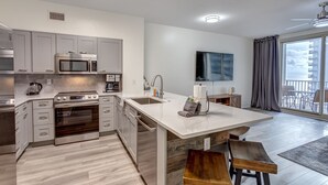 A modern kitchen with stainless steel appliances, a large island, and a view of the balcony.
