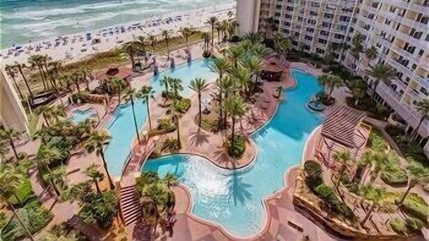A resort with a large pool area surrounded by palm trees and a beach view.