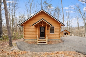 Une cabane en rondins avec un porche à l’avant, une porte avec une enseigne et une fenêtre.