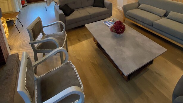 Un salón amplio con un sofá grande, una mesa de centro y un comedor con mesa y sillas. Una escalera conduce a un nivel superior, y un ventanal grande proporciona luz natural.