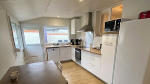 Cocina funcional con armarios blancos, microondas, refrigerador y mesa de madera con sillas.