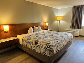 A hotel room with a large bed, two bedside lamps, a nightstand, a floor lamp, and an air conditioning unit.