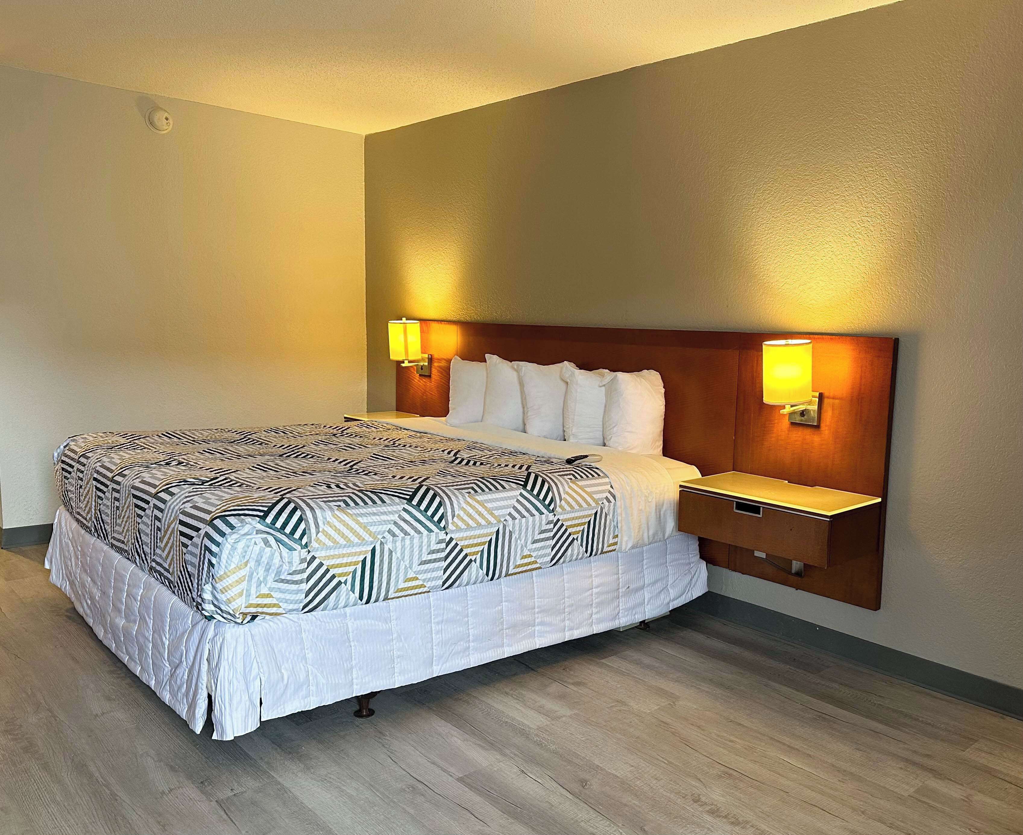 Una habitación de hotel con una cama grande, dos mesitas de noche y un cabecero con lámparas fijadas a la pared.