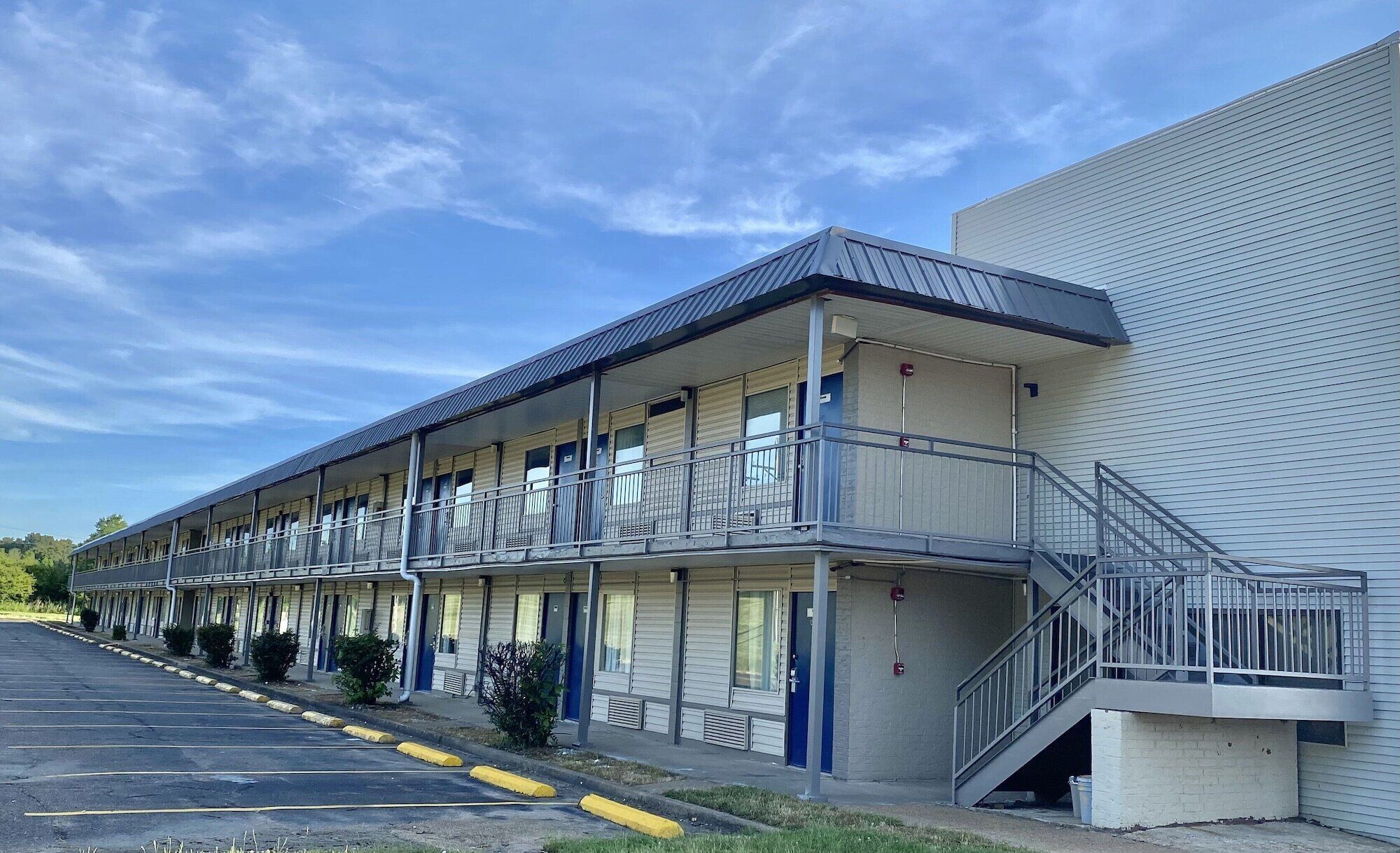 A motel with a row of rooms, a covered walkway, and a stairway leading to an upper level.