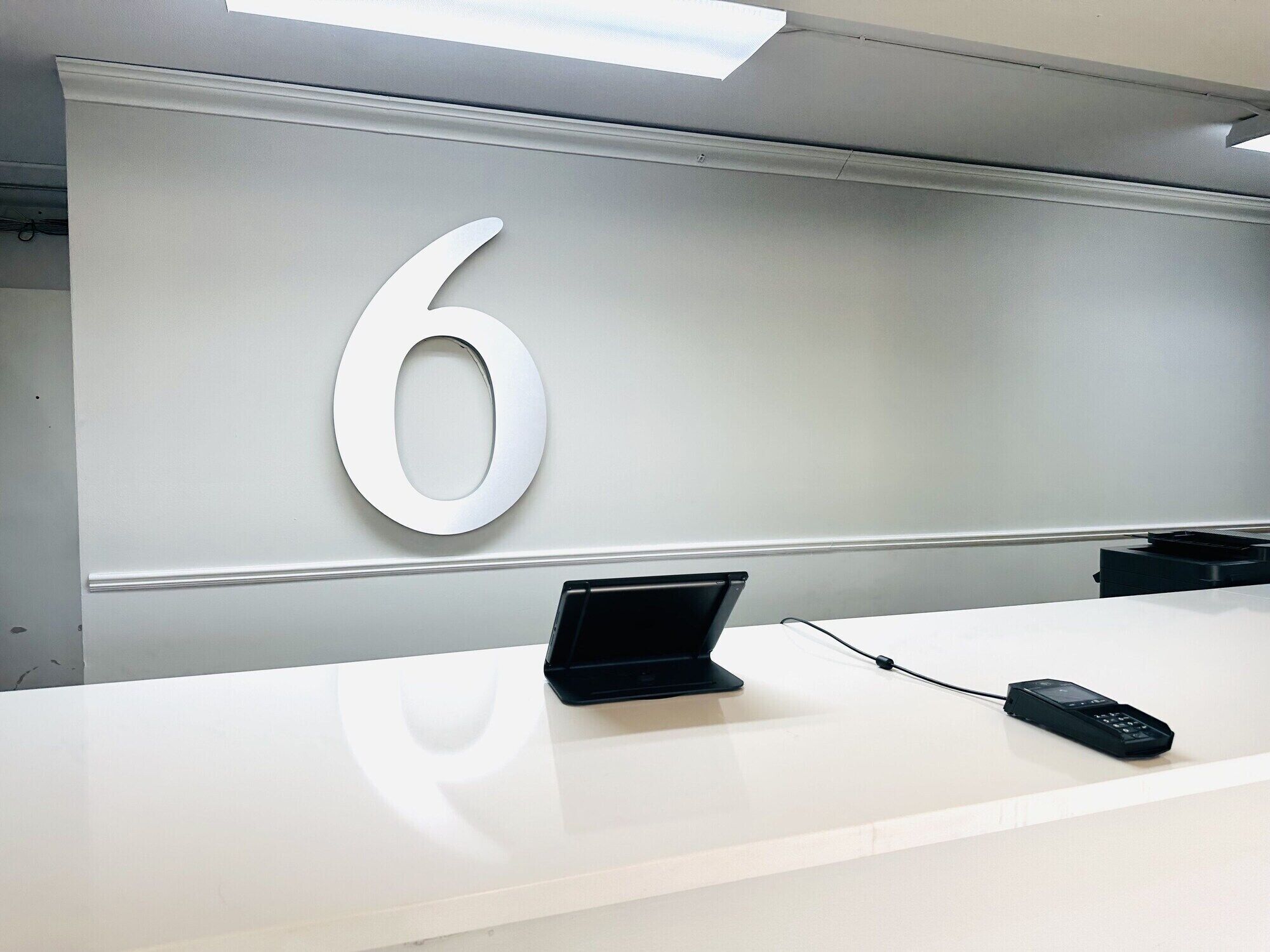 Een receptiebalie met een groot bord met het cijfer 6, een laptop en een telefoon.