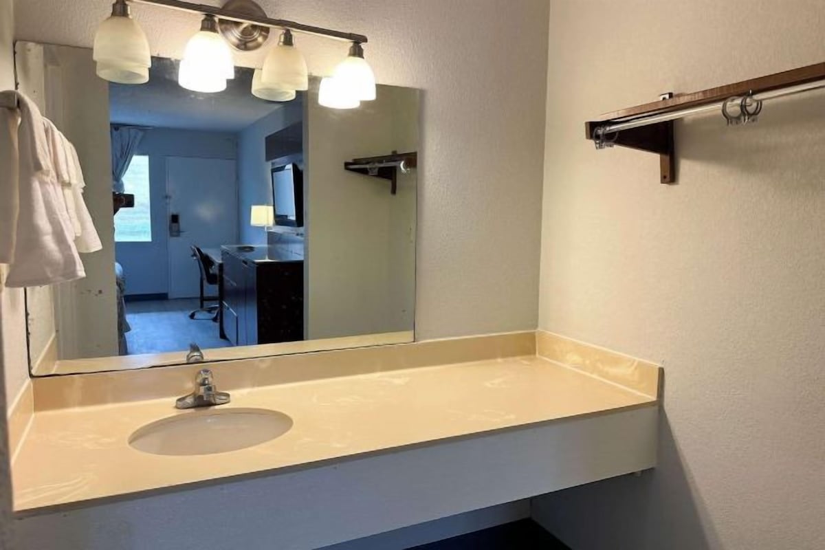 A bathroom with a beige sink, a large mirror, and three pendant lights.