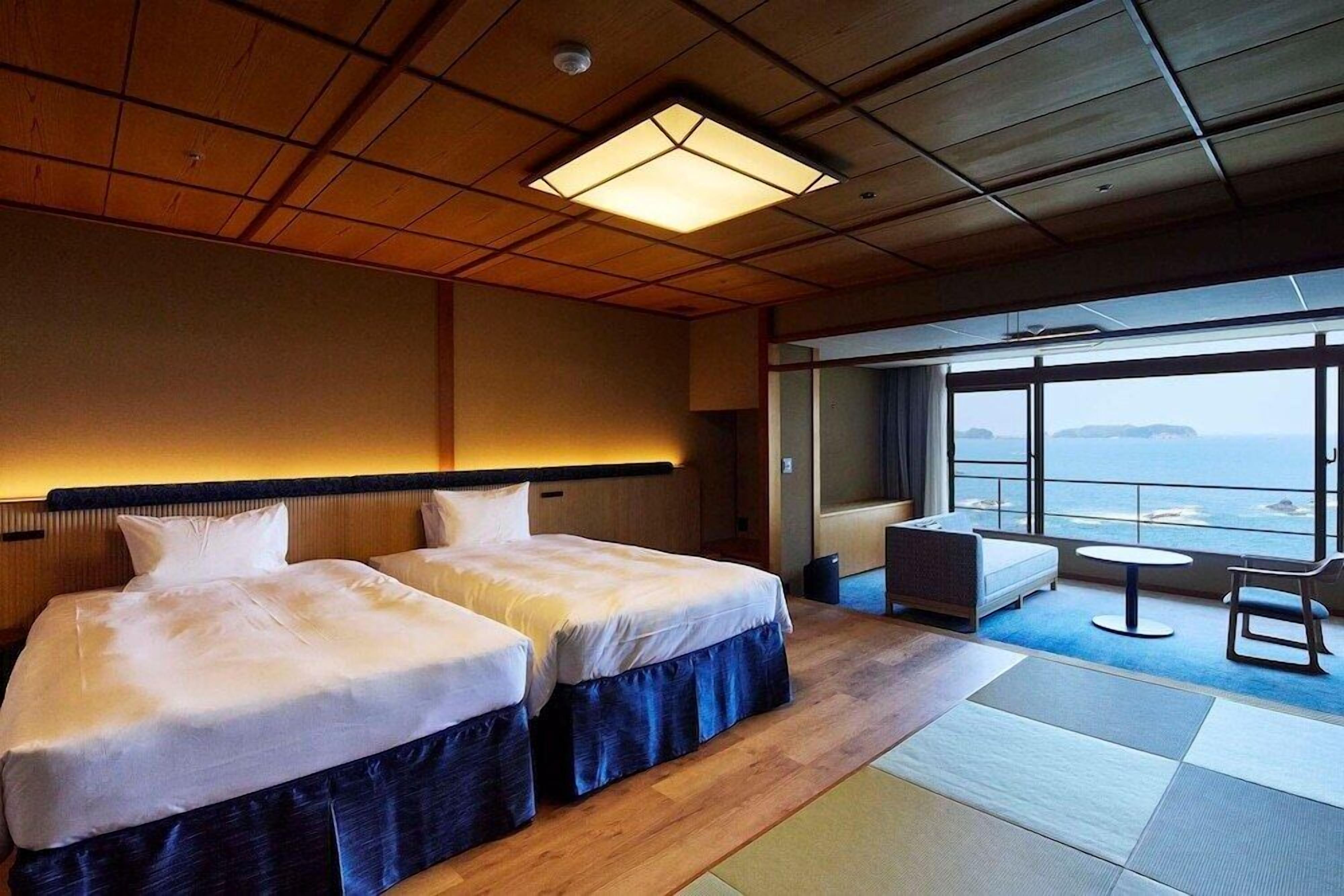 A hotel room with two beds, a sofa, a small table, and a view of the sea.
