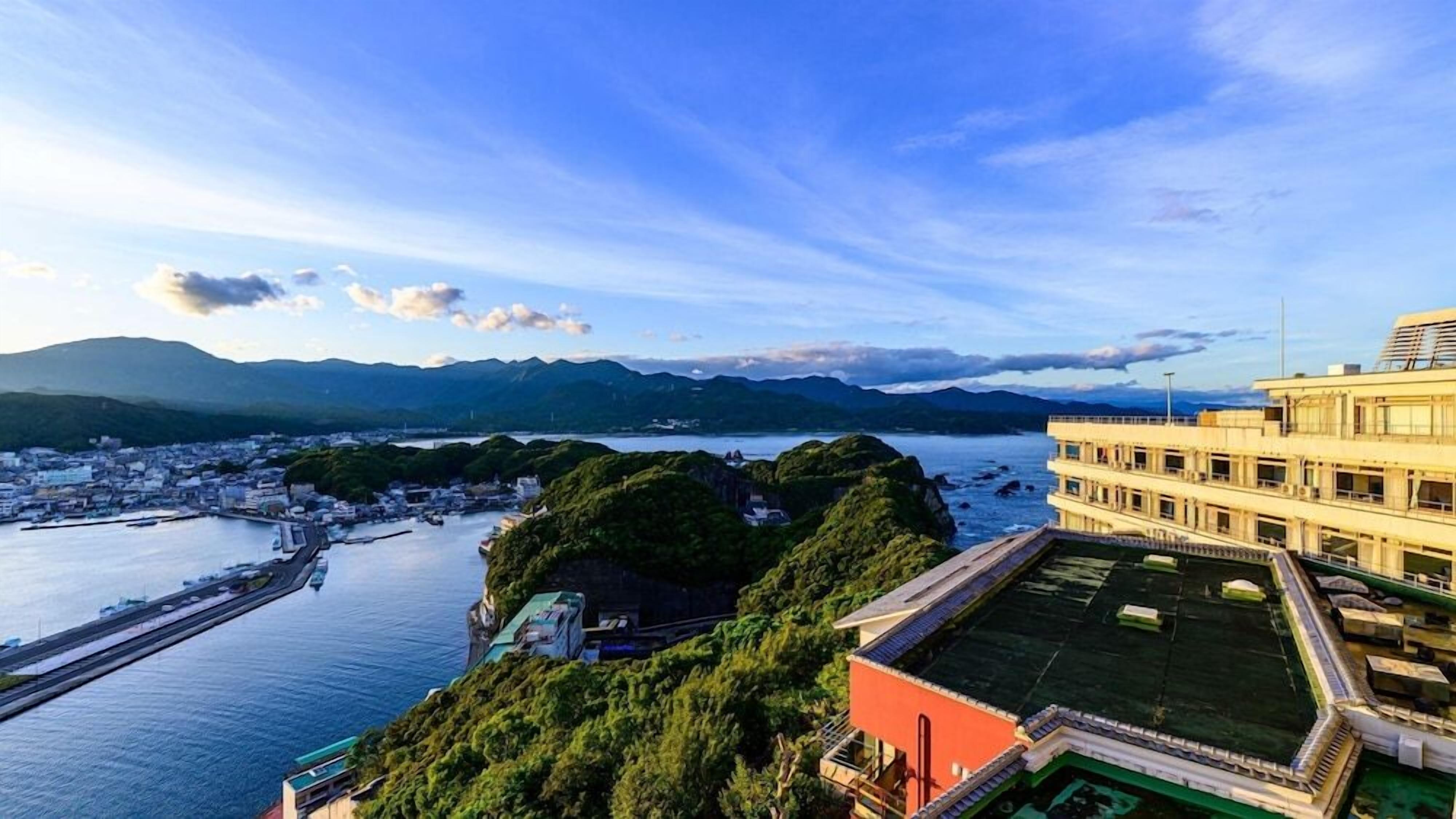 A coastal cityscape with a prominent building featuring a rooftop terrace and a view of the sea.