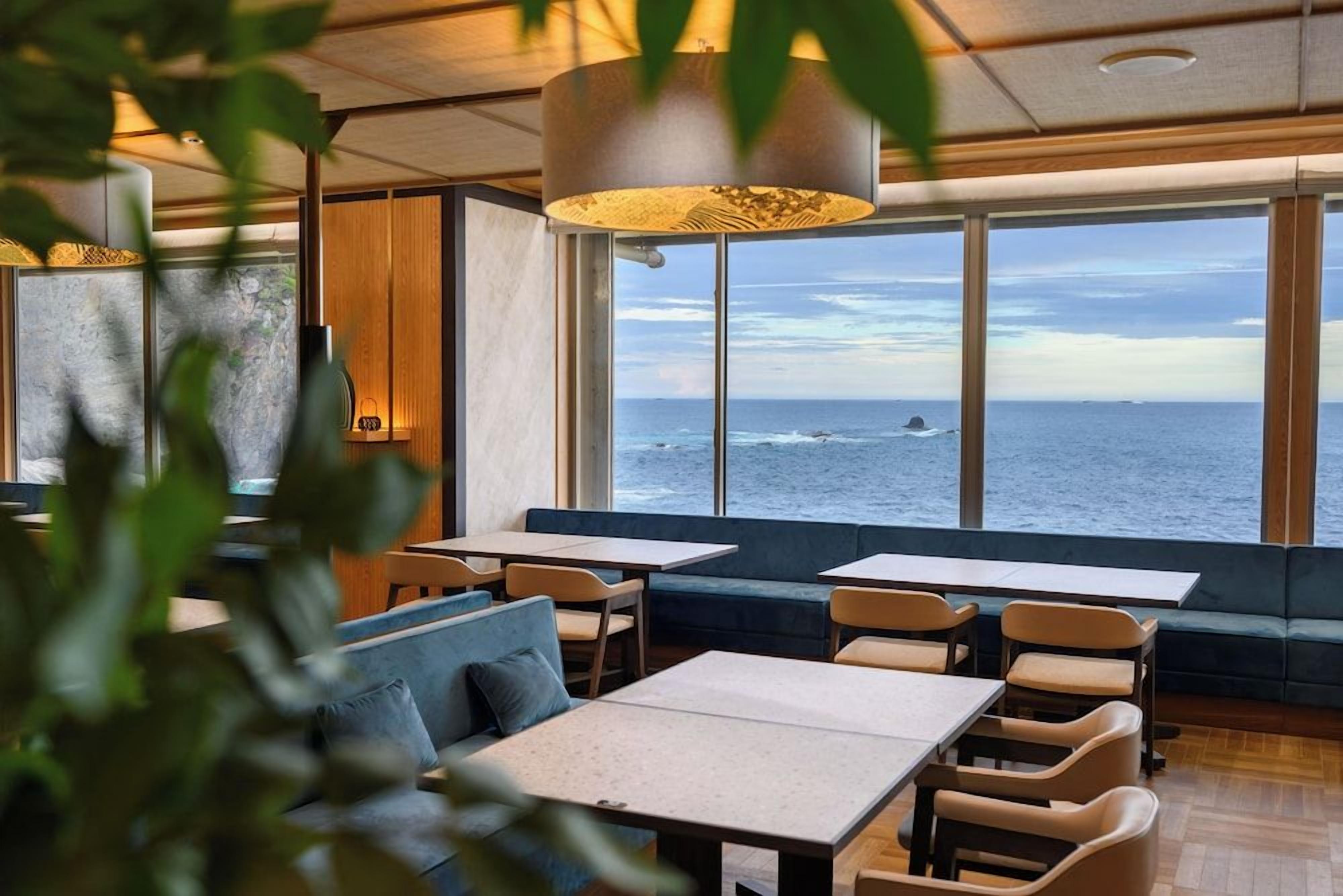 A restaurant with a view of the ocean, featuring tables and seating areas.