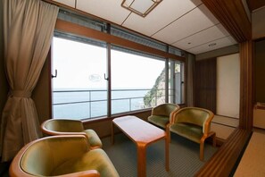 A room with a large window, two chairs, a table, and a view of the sea. - Hotel Urashima (Nachikatsuura)