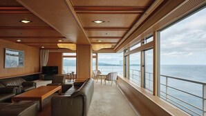 A spacious deck area with a sofa, chairs, a table, and large windows offering a view of the sea. - Hotel Urashima (Nachikatsuura)