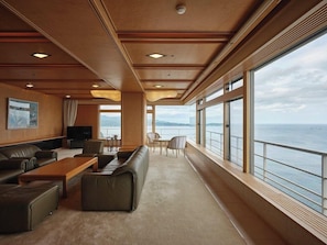 Amplia terraza con sofá, sillas, una mesa y grandes ventanales con vista al mar.