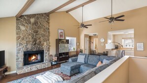 A living room with a stone fireplace, a gray sectional sofa, and a ceiling fan. - Cutest place ever! Fun Airline decor will make you smile! Huge deck! (Jasper)