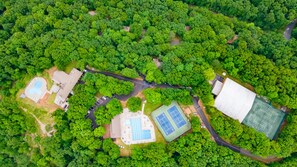 An aerial view of a park with a tennis court, a swimming pool, and a large building.
